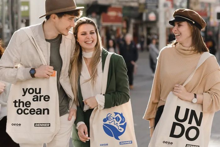Няколко приятели се усмихват един на друг с чанти goodbag от Denner на раменете