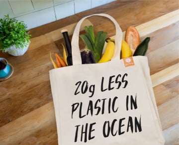 Uma imagem de uma sacola tote goodbag com mantimentos dentro e um design com o texto 20g a menos de plástico no oceano