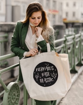 A woman holding a goodbag lifestyle bag with a design 'mermaids hate plastic'